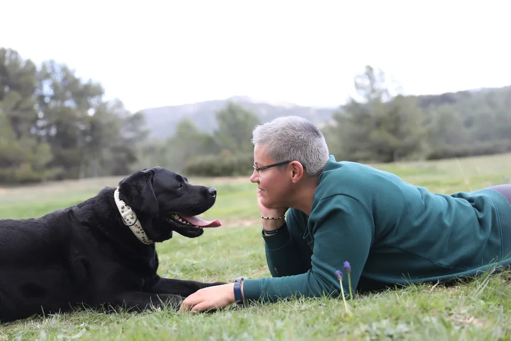 Mónica Corchado tumbada en la hierba frente a un perro negro, trabajando el vínculo con calma